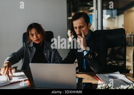 Zwei Experten arbeiten an einem Konferenztisch zusammen und analysieren Dokumente und Laptops in einem modernen Büro Stockfoto