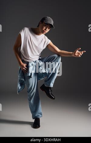Das modische Modell präsentiert sich selbstbewusst in lässiger Jeansbekleidung vor minimalistischem grauem Hintergrund. Stockfoto