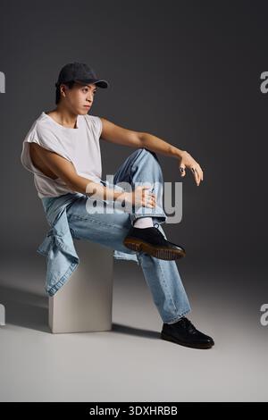Ein junger asiatischer Mann posiert selbstbewusst und betont seine entspannte Mode in einem eleganten Studio. Stockfoto