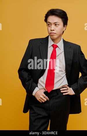 Ein junger asiatischer Mann in Anzug und roter Krawatte posiert selbstbewusst vor gelbem Hintergrund. Stockfoto