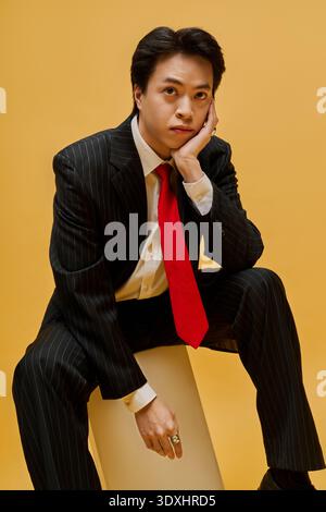 Ein stilvoller junger asiatischer Geschäftsmann in einem Anzug mit roter Krawatte strahlt Vertrauen in ein fröhliches Studio aus. Stockfoto
