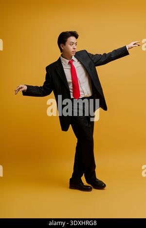 Ein junger asiatischer Geschäftsmann trägt selbstbewusst einen maßgeschneiderten Anzug und eine rote Krawatte vor gelbem Hintergrund. Stockfoto