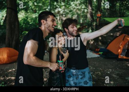Freunde auf einem Campingplatz machen ein Selfie und genießen Drinks im Wald Stockfoto