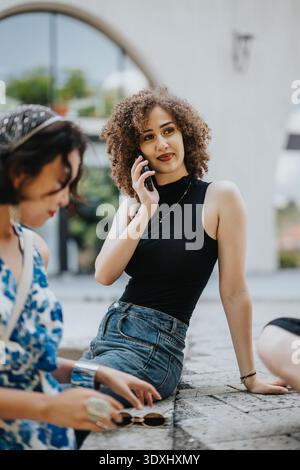 Die junge Frau sitzt auf einem Steinvorsprung und spricht mit einem Freund in der Nähe Stockfoto