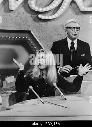 Dieses Werbefoto aus dem Jahr 1971 zeigt Elizabeth Montgomery, bekannt für ihre Rolle in „Bewitched“, als Gast der beliebten Fernsehserie „Password“. Sie spricht animiert in ein Mikrofon, während Gastgeber Allen Ludden hinter ihr steht und das Spiel beobachtet. Das Schwarzweiß-Bild erinnert an die klassische Ära der amerikanischen TV-Unterhaltung. Stockfoto