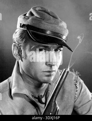 In dieser auffälligen schwarz-weißen Publicity, die noch aus den späten 1950er Jahren stammt, spielt der Schauspieler Nick Adams als Johnny Yuma, der Veteran der Konföderierten Protagonist in der legendären Fernsehserie „The Rebel“. Er trägt einen konföderierten Kepi und hält eine Rauchpistole, die einen robusten und entschlossenen Look ausstrahlt. Das Bild fängt das Wesen der amerikanischen Grenze nach dem Bürgerkrieg ein, eine Zeit dramatischer Veränderungen und individueller Kämpfe. Stockfoto