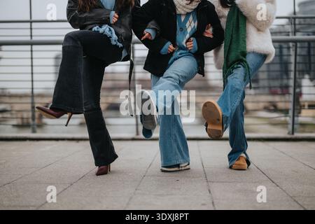 Drei Mädchen zusammen auf einem Stadtrand, heben die Beine in lässigen Winteroutfits Stockfoto
