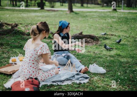Zwei Freunde genießen ein sonniges Picknick im Park mit Büchern, Essen und Tauben in der Nähe Stockfoto