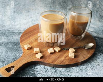 Zwei Gläser Kaffee mit Milch und Zuckerwürfeln auf einem Holzbrett Stockfoto