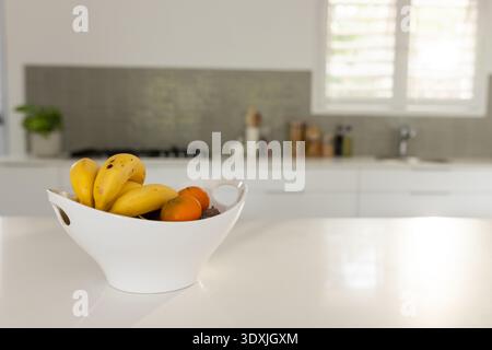 Die Obstschale aus weißer Keramik steht auf der Arbeitsplatte neben dem Gasherd und hält Bananen und Orangen Stockfoto
