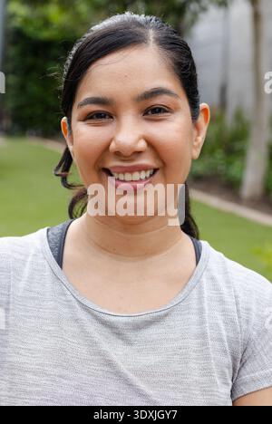 Mittelerwachsene Frau, die im Garten steht, lächelt und ein hellgraues Sporthemd trägt Stockfoto