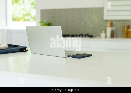 Silberner Laptop, der teilweise offen auf der Insel sitzt, Smartphone und Hülle liegen auf, Gasherd sichtbar Stockfoto