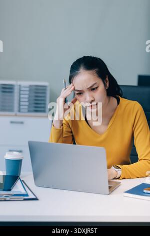 Junge Berufsfrau mit Kopfschmerzen bei der Analyse von Finanzdiagrammen und Diagrammen am Computer, mit berufsbedingtem Stress im modernen o Stockfoto
