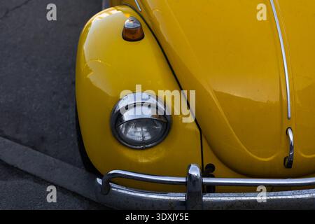 Partielle Front- und Seitenansicht eines gelben Retro-Fahrzeugs mit klassischem Scheinwerferdetail. Stockfoto
