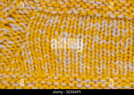 Makroaufnahme aus gelbem und weißem Strickgewebe mit detaillierten Nähten aus Wollgarn und weicher Textur, die handgefertigte Handwerkskunst und gemütliches T-Shirt hervorheben Stockfoto