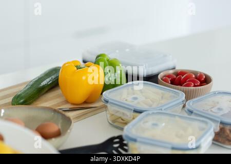 Gelber Paprika sitzt auf hölzernem Schneidebrett auf der Küchentheke mit Essenszubereitungsbehältern Stockfoto