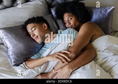 Afroamerikanisches Paar, das sich im Bett hält und mit weißer Bettdecke, goldener Ring sichtbar Stockfoto