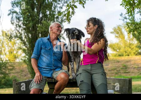 Hundetrainer von Vater und Tochter sitzen an einem Holztisch in einem öffentlichen Park und kuscheln einen italienischen Lagorai-Schäferhund-Welpen Stockfoto