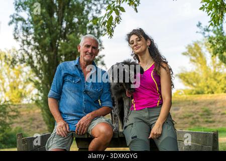 Hundetrainer von Vater und Tochter sitzen auf einem Holztisch und posieren mit einem italienischen Lagorai-Schäferhund-Welpen Stockfoto