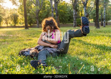 Junge Hundetrainerin, die bei Sonnenuntergang in einem öffentlichen Park auf dem Gras sitzt und Spaß mit ihrem italienischen Schäferhund Lagorai hat Stockfoto