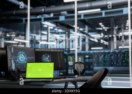 Laptop und Computer mit grünem Bildschirm im Rechenzentrum, die für Systeme mit künstlicher Intelligenz erforderliche Server-Racks überwachen. Chroma Key Notebook und PC im Arbeitsbereich zur Überwachung von Server-Hub-Geräten Stockfoto