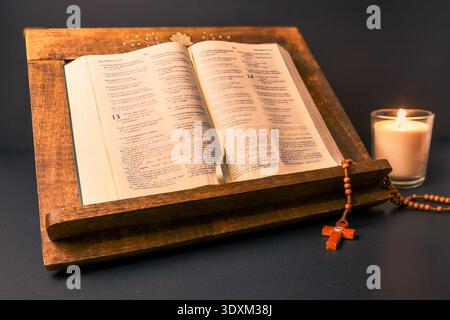 Öffnen Sie die Bibel auf hölzernem Rednerpult mit Rosenkranz und Kerze. Katholische Hingabe, Gebet, Spiritualität, Fastenzeit und Stillleben in der Karwoche. Stockfoto
