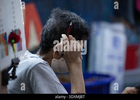 BANGKOK, THAILAND-4. Februar 2026: Senior man-Verkäufer mit kurzen Haaren auf dem Markt, offenes tropisches Straßenleben, Seitenprofil Stockfoto