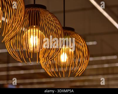 Moderne Pendelleuchten mit goldenen Lampenschirmen aus Drahtkäfig und Vintage-Edison-Lampen, die in einem warmen, gemütlichen Interieur leuchten. Elegante Wohnbeleuchtung im Loft-Stil Stockfoto