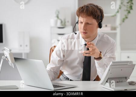Junger Geschäftsmann, der am Schreibtisch im Büro mit Headset und Laptop arbeitet Stockfoto