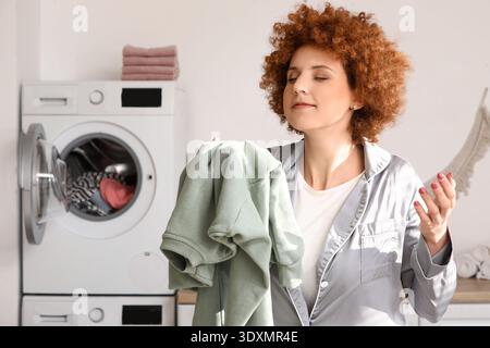 Rothaarige junge Frau, die saubere Wäsche im Zimmer riecht Stockfoto