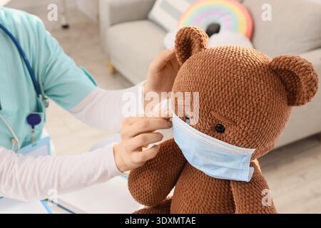 Kinderärztin und Spielzeugbär mit medizinischer Maske in der Klinik, Großaufnahme Stockfoto