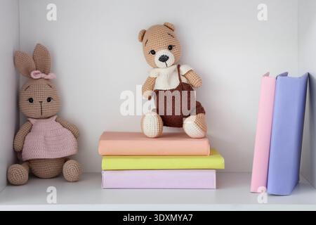 Regal mit Büchern und Spielzeug in der Nähe der weißen Wand im Kinderzimmer Stockfoto