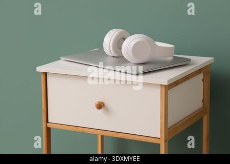 Weißer Nachttisch mit modernem Laptop und Kopfhörern auf grünem Hintergrund Stockfoto