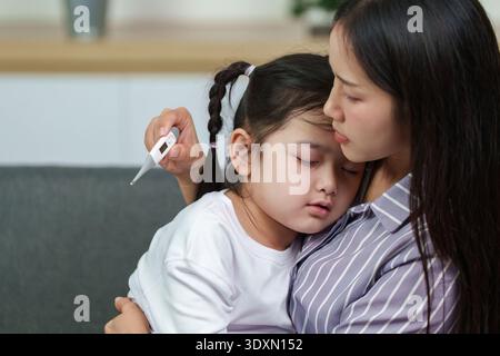 Mutter, die die Temperatur der kranken Tochter überprüft. Fürsorgliche Gesundheitsförderung. Stockfoto