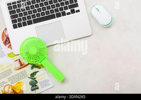 Tragbarer grüner Elektroventilator, Laptop und Magazin auf weißem Grunge-Hintergrund Stockfoto