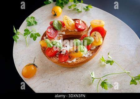 Runde Bruschetta mit roten und gelben Kirschtomaten und Ziegenkäse auf Marmorplatte. Agrarprodukte, knuspriges Brot. Essen und gesunde Ernährung. Stockfoto