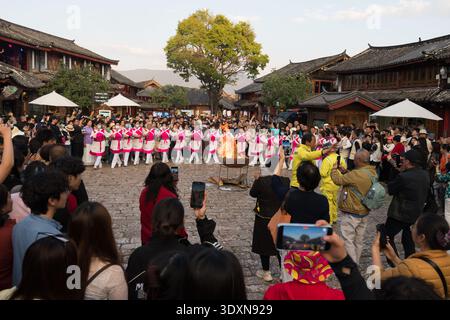 Lijiang, Yunnan, China – 10. April 2025: Naxi-Künstler in traditionellen Kostümen tanzen mit Feuerrequisiten während einer kulturellen Veranstaltung in überfüllten s Stockfoto