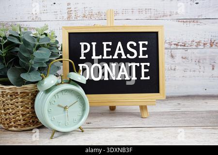 Bitte spenden Sie Text auf Tafel mit Wecker auf hölzernem Hintergrund Stockfoto