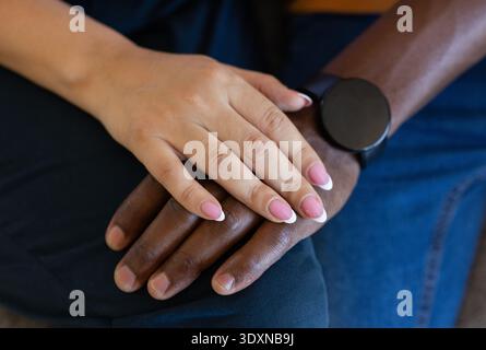 Verschiedene Paare zeigen Hände, ruhen sich drinnen auf dem Schoß aus, tragen schwarze Smartwatch und rosa Maniküre Stockfoto