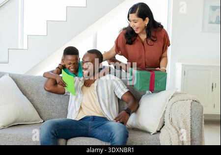 Verschiedene Familieneltern Teenager-Sohn, der zu Hause auf grauem Sofa sitzt, teilen Greencard und Geschenk Stockfoto
