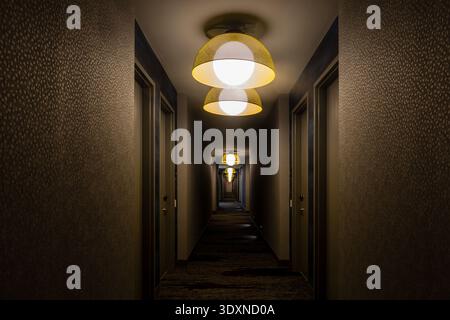Langer schmaler Hotelflur, schwach beleuchtet mit Lampen und Teppichboden. Stockfoto