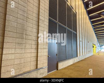 Ein Gebäude zeigt sein Äußeres mit einer Metalltür, die in eine Wand aus Betonblöcken eingelassen ist. Die Wand verfügt über Lattenbleche zur Belüftung. Die Einstellung ist A Stockfoto