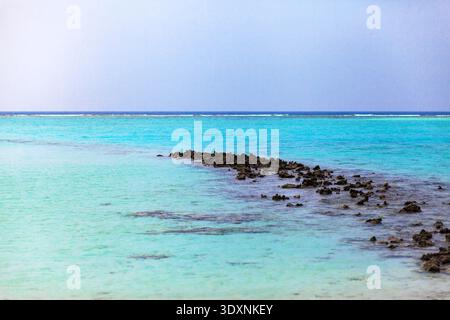 Kristallklares Wasser trifft auf ein ruhiges, sonniges Ufer. Die schmale Rifflinie zieht sich sanft ins Blau. Sanftes Licht leuchtet über dem ruhigen, türkisfarbenen Meer. Großer Horizont bl Stockfoto