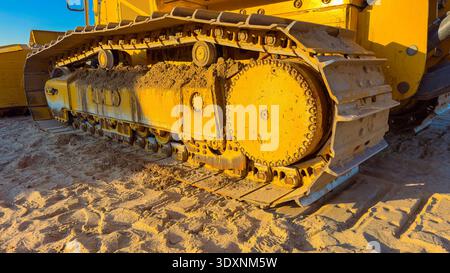 Auf einer Baustelle ist eine große Anlage aktiv, deren Schienen mit Sand bedeckt sind. Die Sonne scheint hell auf die Maschine, während sie arbeitet Stockfoto