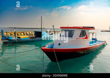 Helle Sonne leuchtet über dem ruhigen türkisfarbenen Meer. Zwei farbenfrohe Fischerboote schweben sanft am Dock. Ein Boot ist weiß mit rotem Besatz, robust und bereit. Die Othe Stockfoto