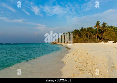 Ruhiges türkisfarbenes Wasser trifft auf weichen weißen Sand. Palmen säumen die ruhige Küste. Der Himmel ist hellblau mit wackeligen Wolken. Der Strand lädt zum Entspannen ein Stockfoto