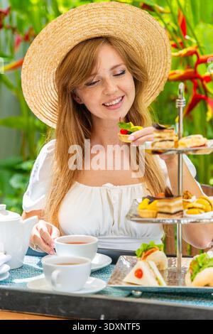 Frau genießt Nachmittagstee im Garten, trägt Sonnenhut, Stockfoto