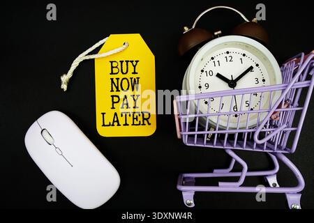 Jetzt kaufen, später bezahlen Text mit Preisschild, optischer Maus, Rollwagen und Wecker auf schwarzem Hintergrund, Shopping Online Konzept Stockfoto