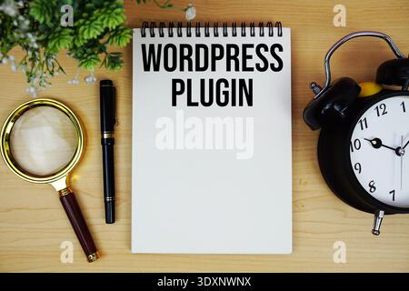 WordPress Plugin Text geschrieben auf Notizblock mit Wecker und Lupe flach auf hölzernem Hintergrund Stockfoto