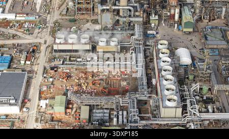 Aus der Vogelperspektive einer weitläufigen Industrieanlage mit Dampf aus Kühltürmen und einem Netz von Pipelines im Kontrast zu den Erdtönen von Co Stockfoto